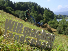 Eine der bayernweiten Aktionen des Deutschen Verbands für Landschaftspflege zur Fördermittel-Problematik: Das Logo „WIR machen Landschaft“ wurde auf verschiedensten Naturschutzflächen fotografiert, die nur mit Fördermitteln erhalten werden können. Hier: Heubergung mit Schubgabel auf dem Vogelberg am Forggensee.